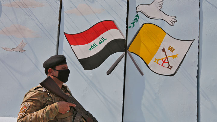 Un miembro de las fuerzas iraquíes se encuentra junto a un mural que representa las banderas unidas de Irak y la Santa Sede dibujadas en un muro explosivo fuera de la Iglesia católica siríaca de Nuestra Señora de la Liberación. / Foto: AFP