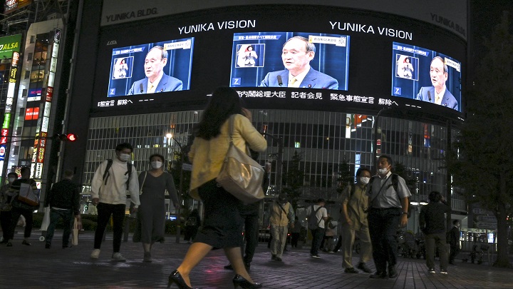 Peatones en calle ven una transmisión de televisión del primer ministro de Japón, Yoshihide Suga, anunciando el levantamiento del estado de emergencia por coronavirus./ AFP 