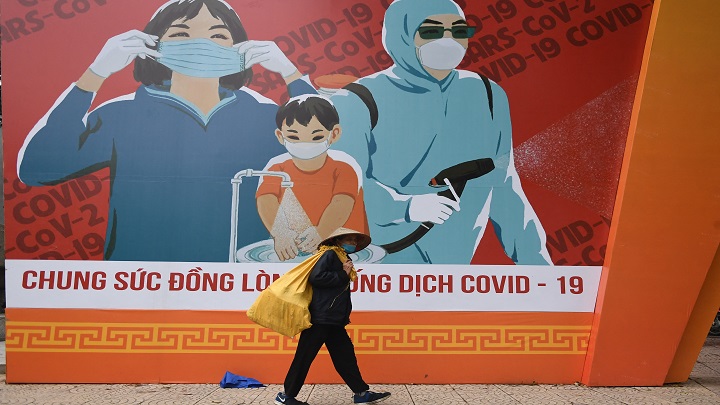una mujer pasa junto a una valla publicitaria con información sobre cómo prevenir la propagación del coronavirus Covid-19 en Hanoi./AFP