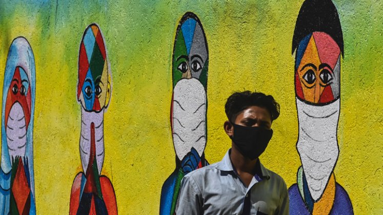 Un hombre pasa junto a un mural que muestra a personas de varias religiones agradeciendo a los guerreros del coronavirus de primera línea, en Mumbai. / Foto: AFP