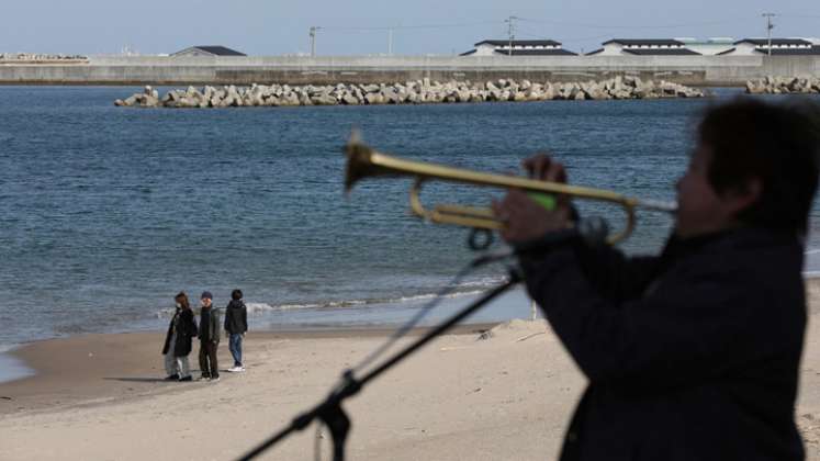 Un residente local toca una trompeta para las víctimas del terremoto y tsunami en una playa en Soma el 11 de marzo de 2021, el décimo aniversario del terremoto de magnitud 9.0 que provocó un tsunami y un desastre nuclear. / Foto: AFP