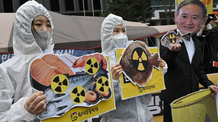 Activistas ambientales surcoreanos con ropa protectora y una máscara (R) del primer ministro de Japón, Yoshihide Suga, sostienen imágenes de peces con carteles de advertencia de radiactividad durante una protesta contra la decisión de Japón de liberar las aguas residuales de Fukushima, cerca de la embajada japonesa en Seúl. / Foto: AFP
