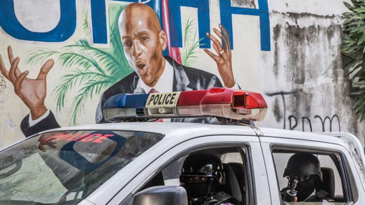 Un convoy policial pasa junto a una pared pintada con la imagen del presidente haitiano Jovenel Moise, asesinado por mercenarios armados. / Foto: AFP