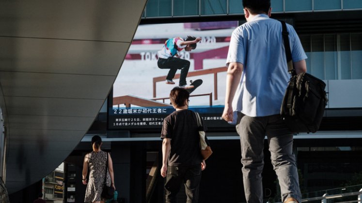 La gente camina frente a un tablero de anuncios eléctrico que muestra al japonés Yuto Horigome, el primer medallista de oro en la calle masculina de Skateboarding de los Juegos Olímpicos de Tokio 2020, en Tokio, este domingo. / Foto AFP